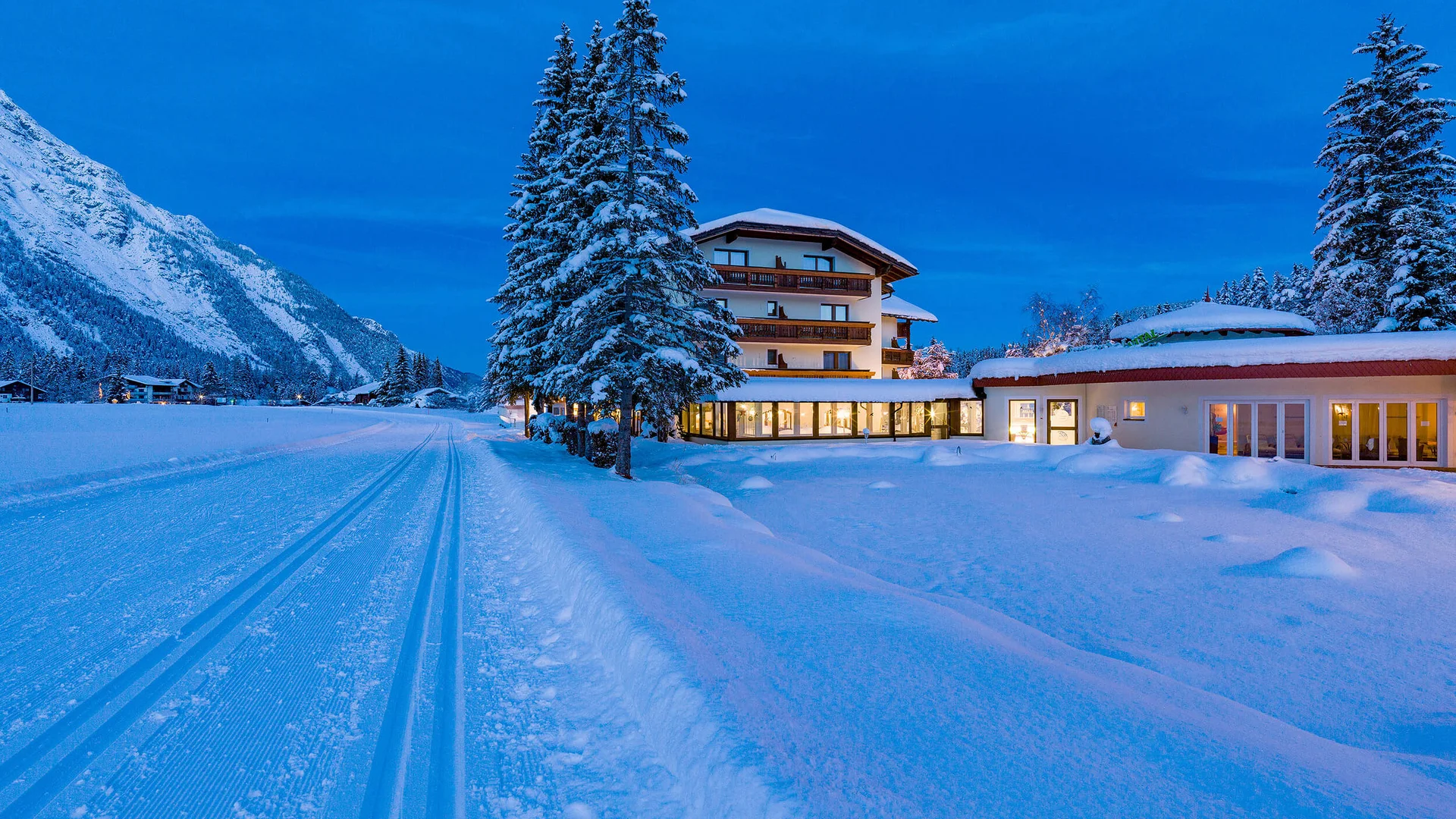 Snow-covered hotel with lit windows and snowy trees at dusk