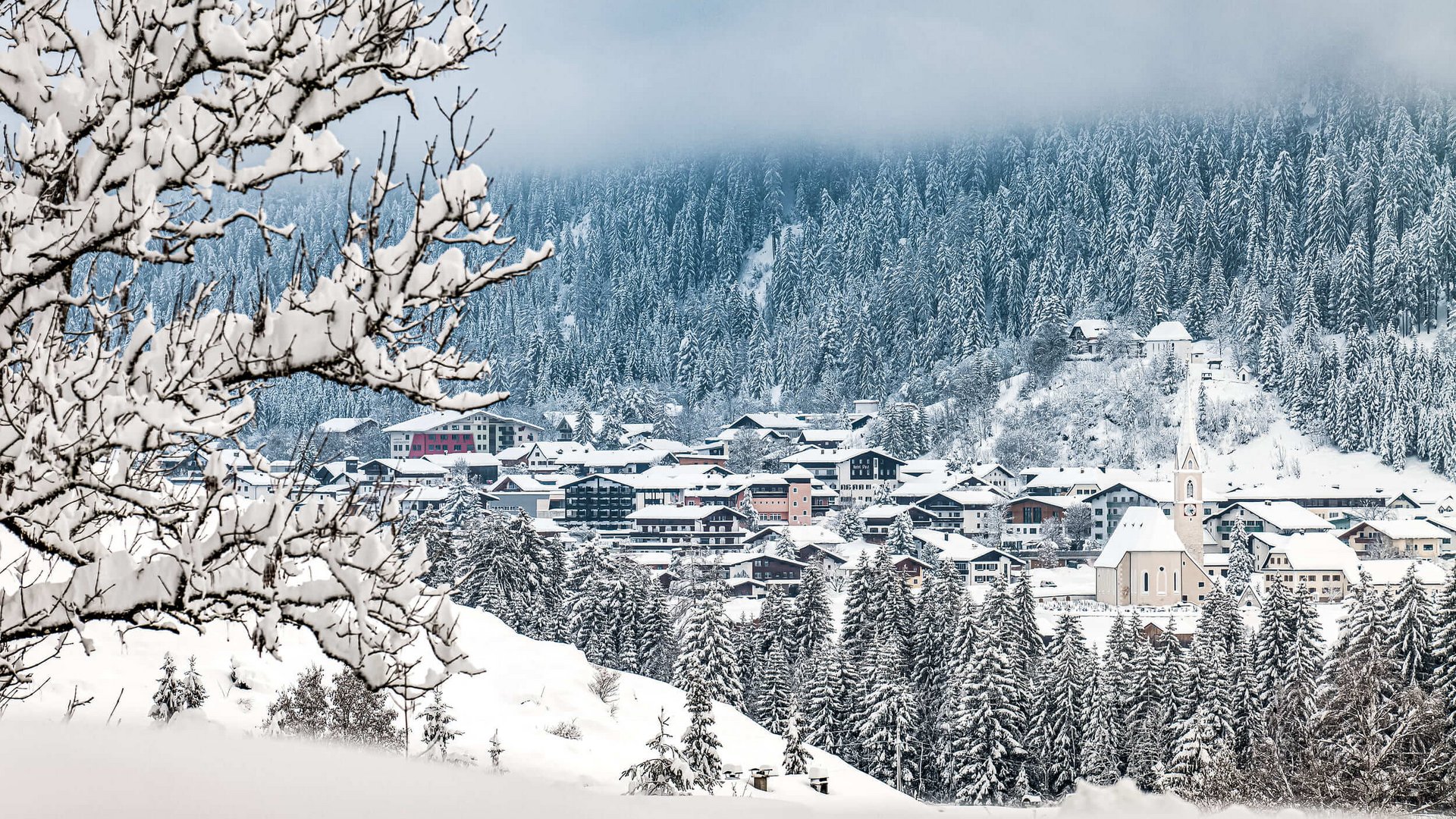 Snow-covered village with forest and cloudy sky in winter