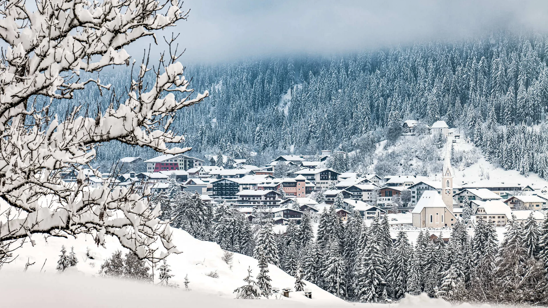 Trails & trail reports © Lechtal Tourismus / Radomir Gabric Snow-covered village with forest and cloudy sky in winter