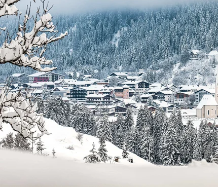 Lechtal © Lechtal Tourismus / Radomir Gabric Schneebedecktes Dorf vor verschneitem Wald und bewölktem Himmel