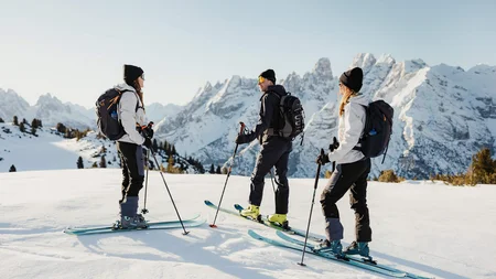 Three skiers standing on snow with mountains in the background