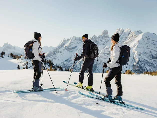 Three skiers standing on snow with mountains in the background