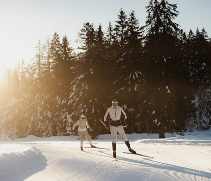 Bergwelten Nordic Experience © Alex Moling Zwei Skifahrer beim Langlauf auf verschneiter Strecke mit Wald im Hintergrund