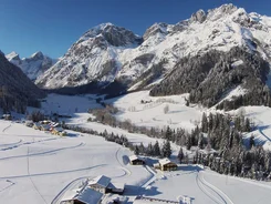 Snow-covered alpine landscape with houses and pine trees under clear sky