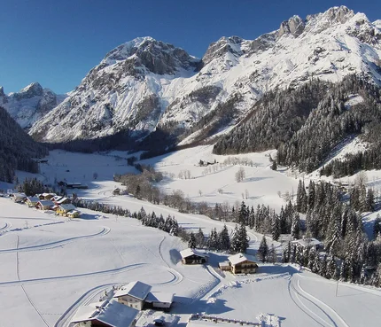 Snow-covered alpine landscape with houses and pine trees under clear sky