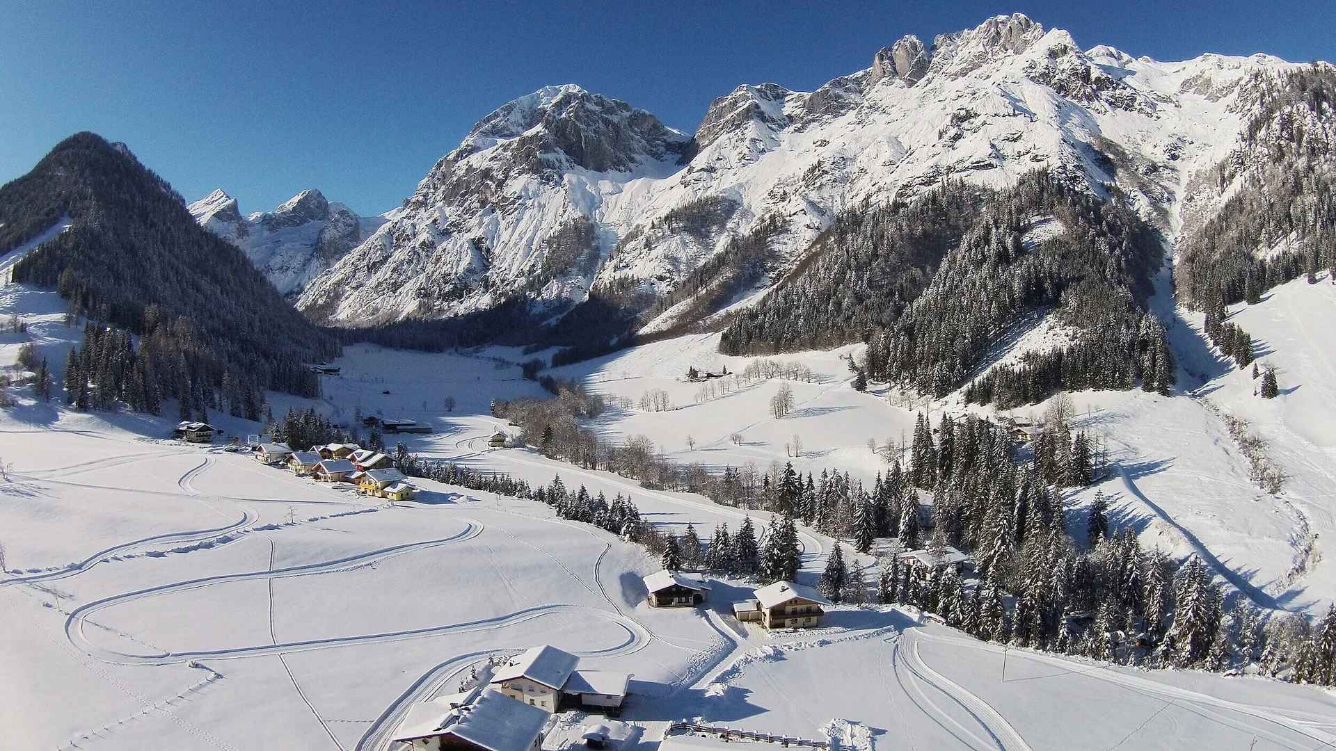 Cross-country skiing holiday in the Tennengau region Snow-covered alpine landscape with houses and pine trees under clear sky