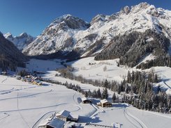 Schneebedeckte Alpenlandschaft mit Häusern und Nadelwäldern unter klarem Himmel