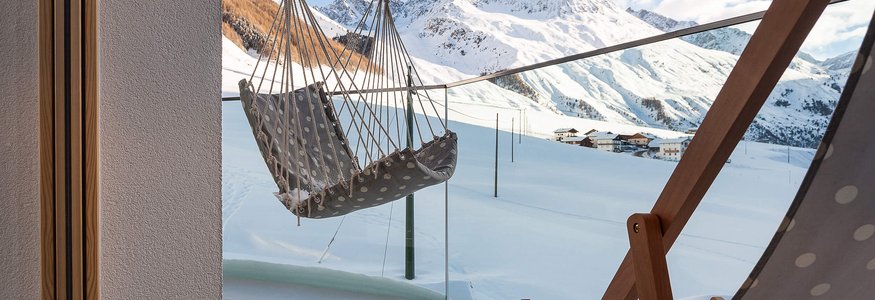 Terrasse mit Hängesessel und Liegestuhl vor schneebedeckten Bergen