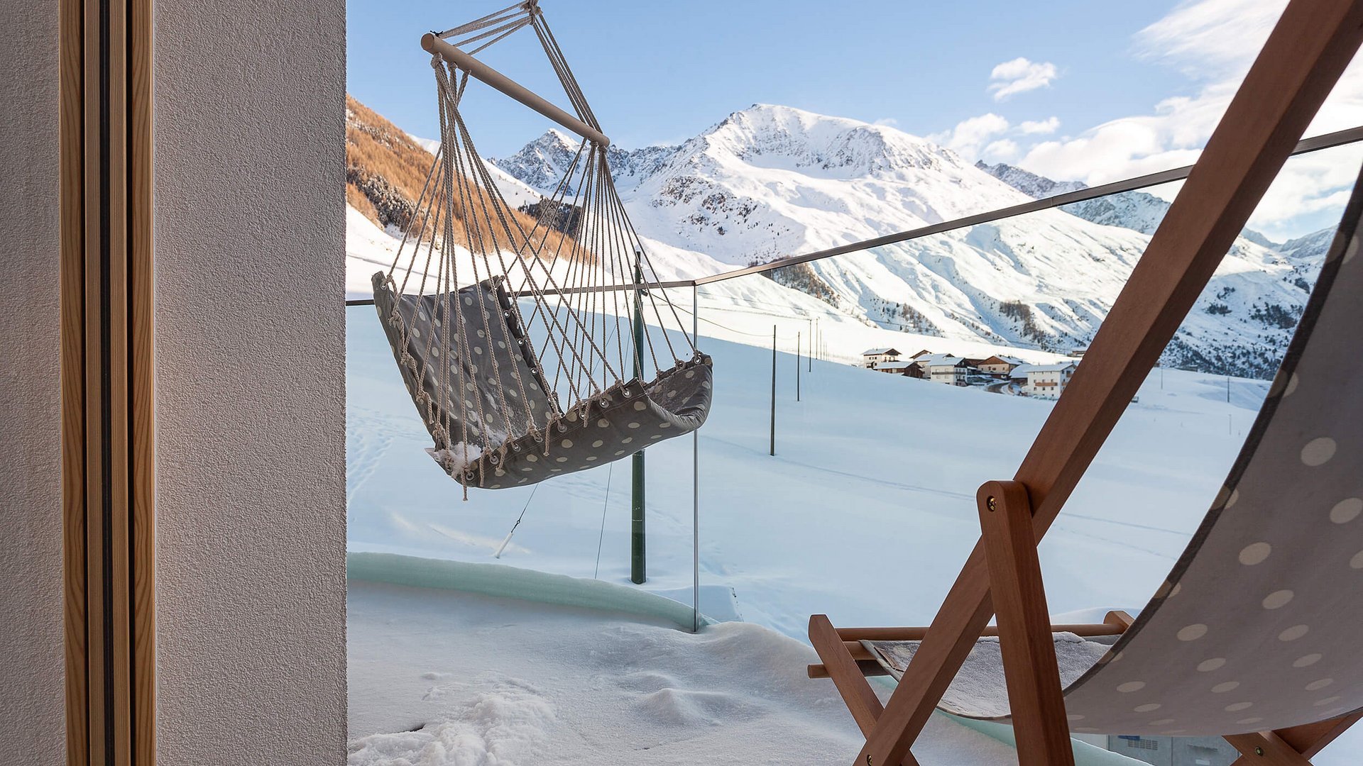 Terrasse mit Hängesessel und Liegestuhl vor schneebedeckten Bergen