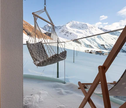Terrasse mit Hängesessel und Liegestuhl vor schneebedeckten Bergen