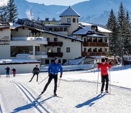 Langläufer vor dem Hotel Karwendel mit verschneiten Bergen im Hintergrund
