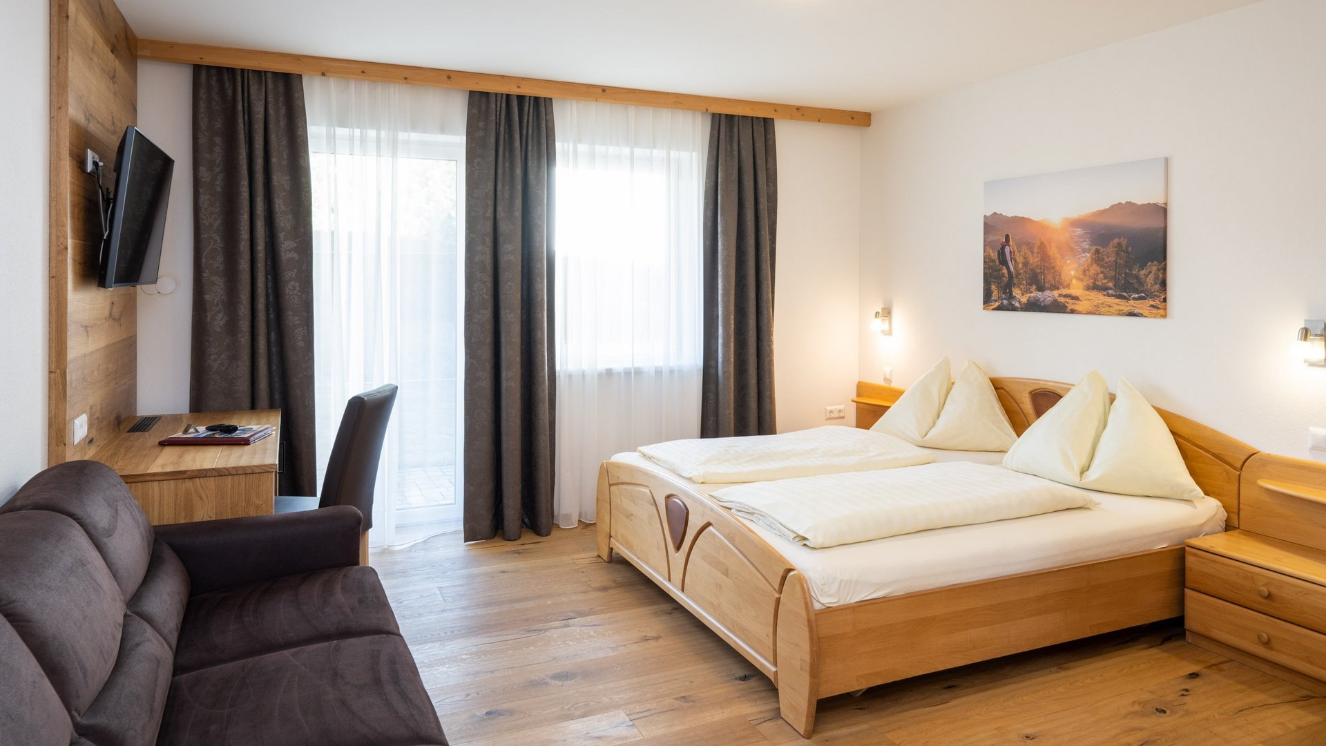 Bright hotel room with double bed, sofa, desk, and TV