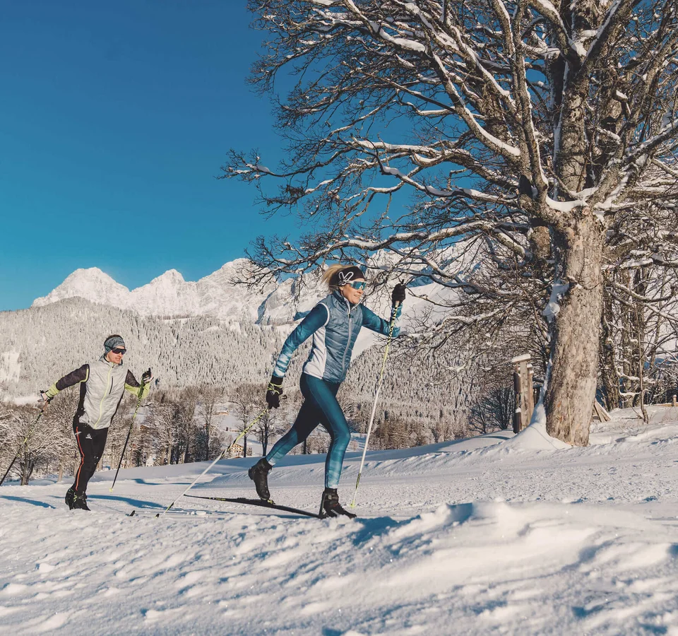 Two people cross-country skiing in snowy mountain landscape under clear sky