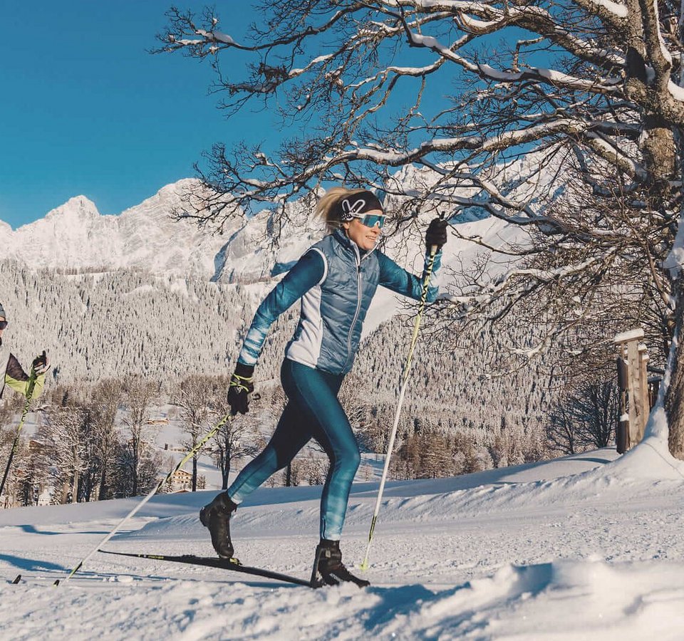 Zwei Personen beim Langlaufen vor verschneiten Bergen und klarem Himmel