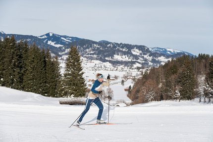 Frau beim Langlauf im verschneiten Gebirge mit Tannenbäumen im Hintergrund