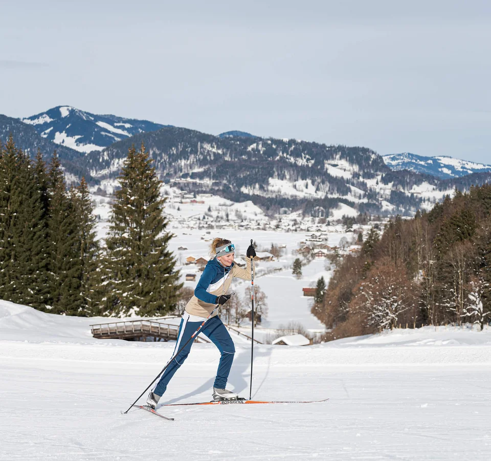 Frau beim Langlauf im verschneiten Gebirge mit Tannenbäumen im Hintergrund