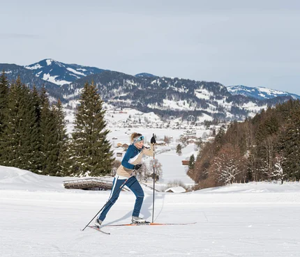 Frau beim Langlauf im verschneiten Gebirge mit Tannenbäumen im Hintergrund