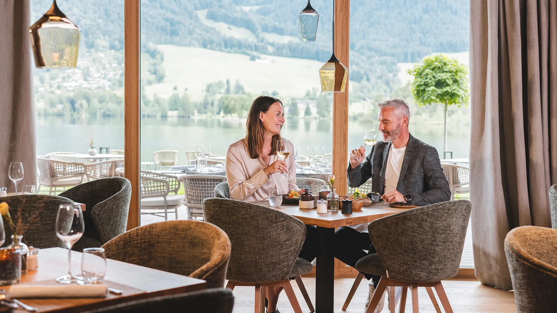 Paar trinkt Wein und genießt Blick auf See und Berge im Restaurant
