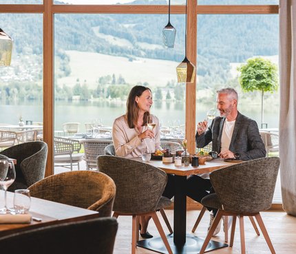 Paar trinkt Wein und genießt Blick auf See und Berge im Restaurant