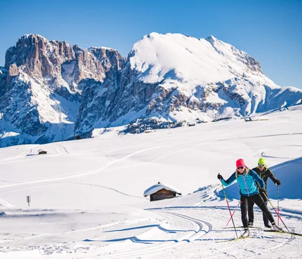 Zwei Langläufer bei sonnigem Wetter vor schneebedeckten Bergen