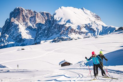 Zwei Langläufer bei sonnigem Wetter vor schneebedeckten Bergen