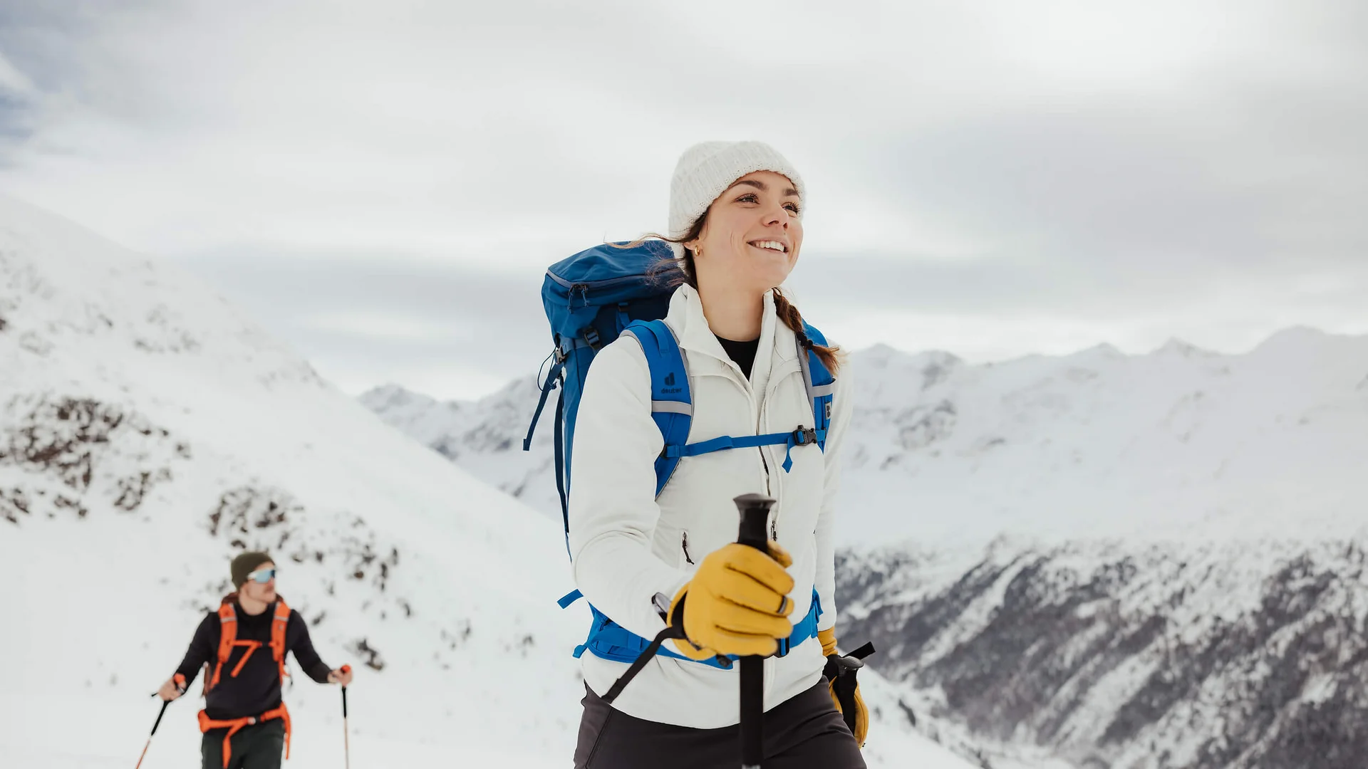 Frau und Mann wandern mit Rucksack und Stöcken im schneebedeckten Gebirge