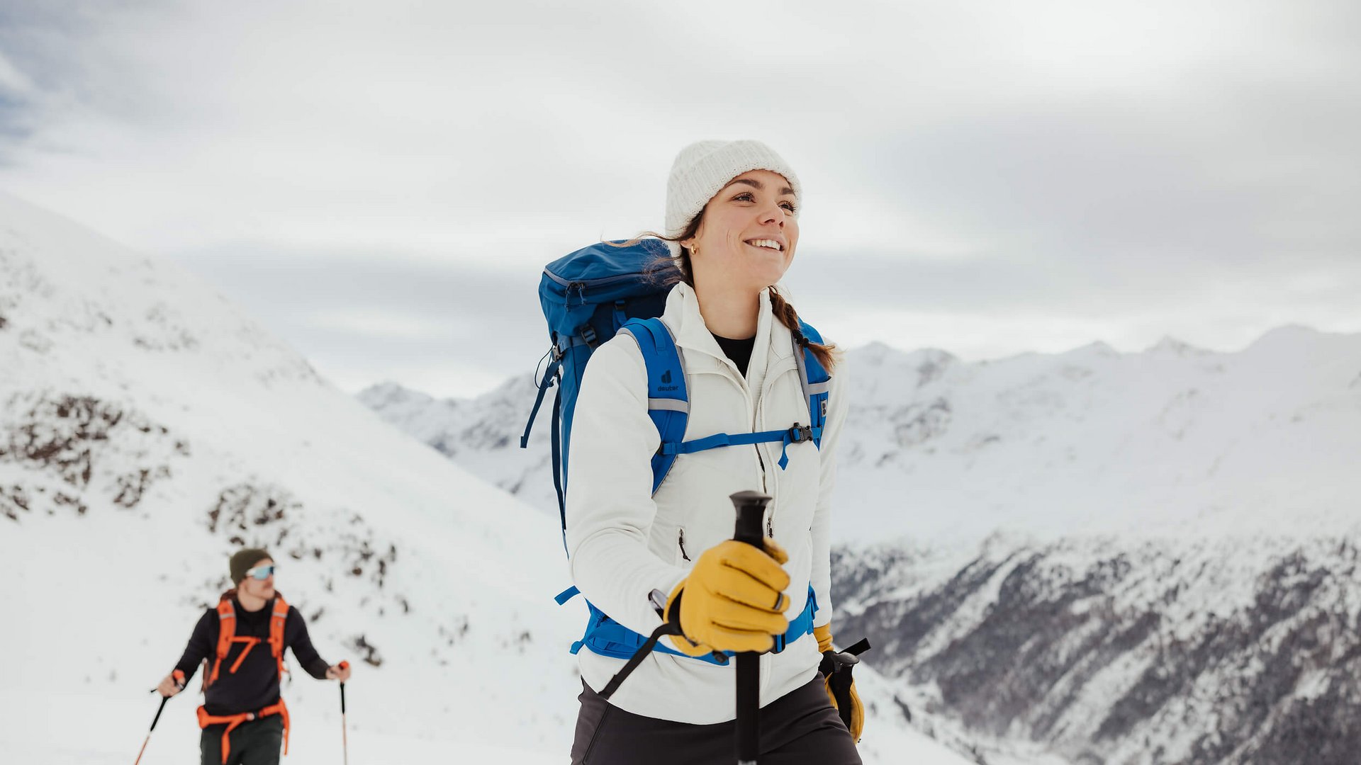 Frau und Mann wandern mit Rucksack und Stöcken im schneebedeckten Gebirge