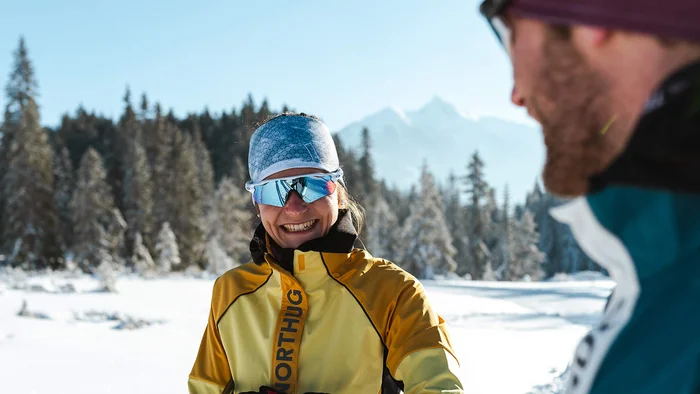 Frau im gelben Skianzug und reflektierender Brille im Schnee mit Mann im Vordergrund