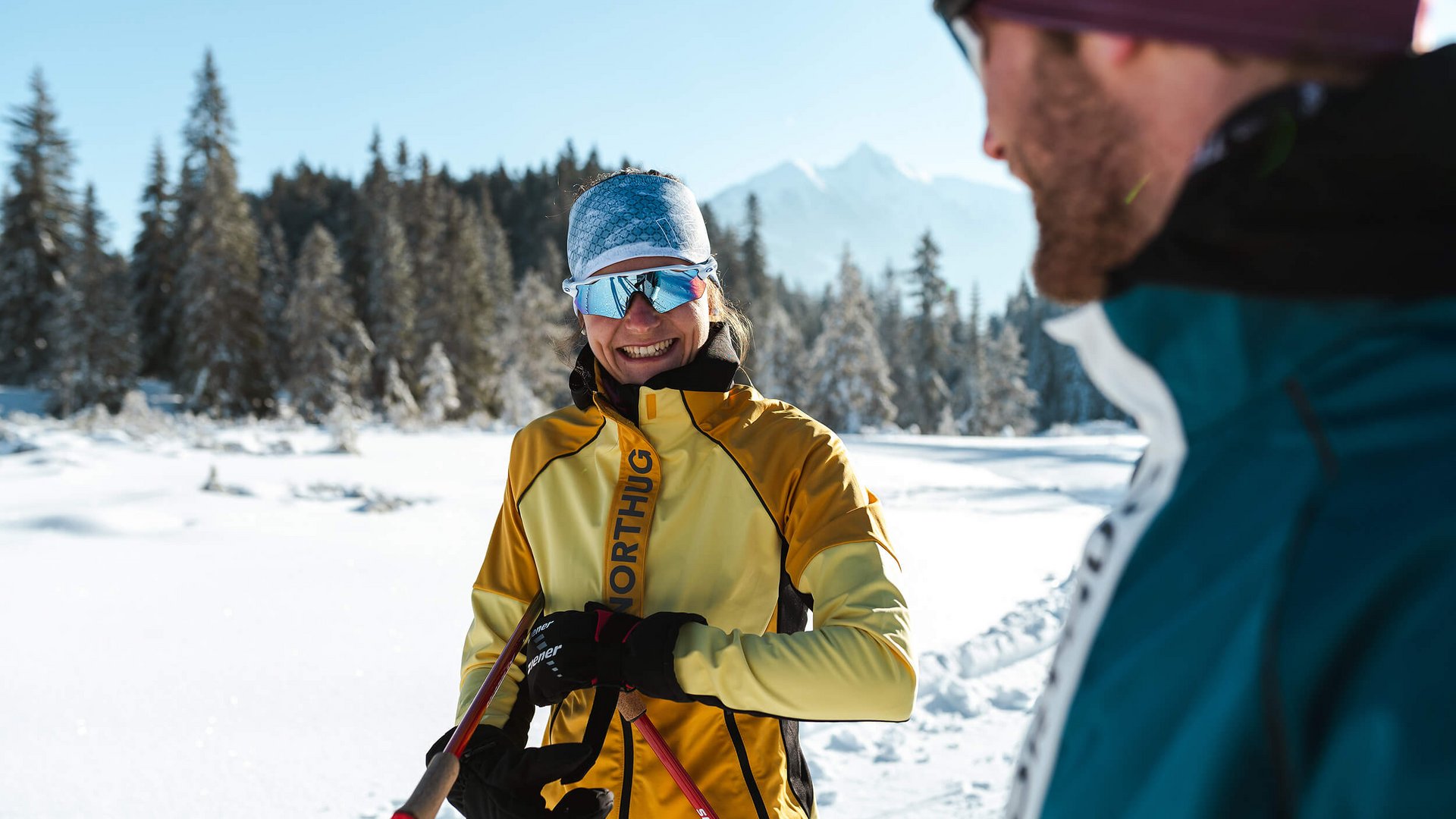 Woman in yellow ski suit and reflective goggles in snow with man in foreground