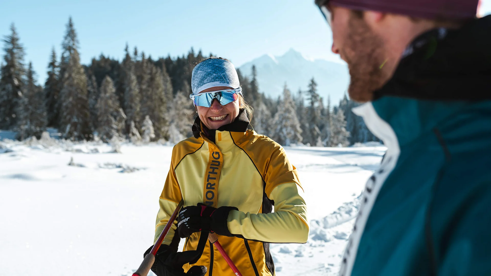 Frau im gelben Skianzug und reflektierender Brille im Schnee mit Mann im Vordergrund