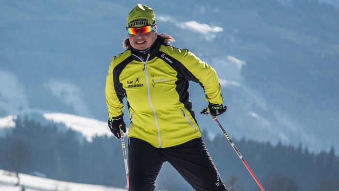 Person beim Langlaufen auf verschneiter Winterlandschaft mit Bergen im Hintergrund