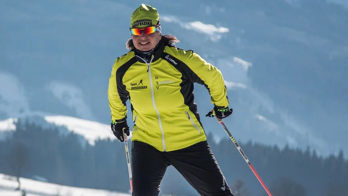 Person beim Langlaufen auf verschneiter Winterlandschaft mit Bergen im Hintergrund
