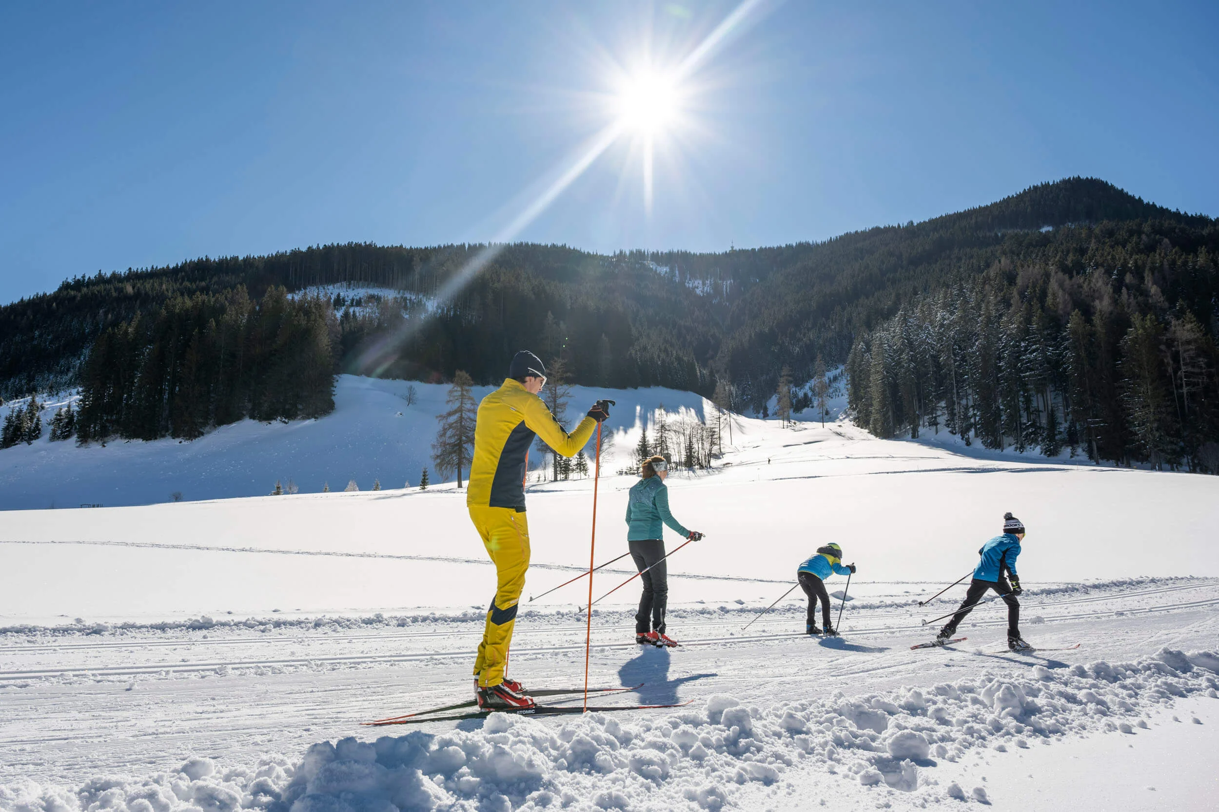 Familie beim Langlaufen auf verschneiter Berglandschaft bei Sonnenschein