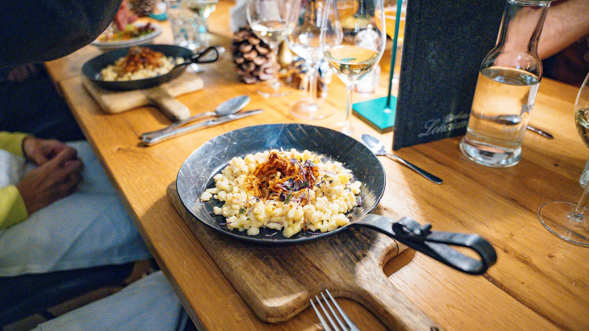 Schwarze Pfannen mit Spätzle und Zwiebeln auf Holzbrett und gedecktem Tisch