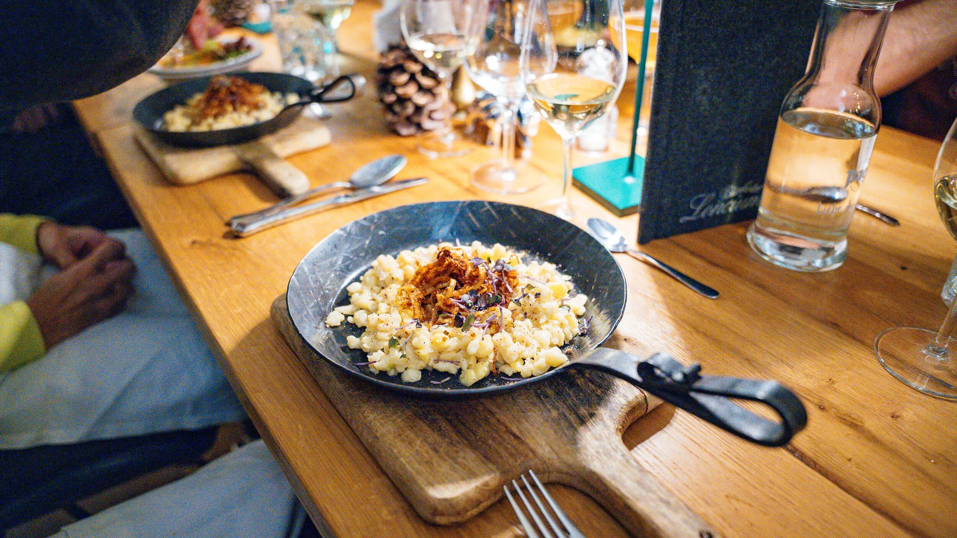 Black pans with spaetzle and onions on wooden board and set dining table