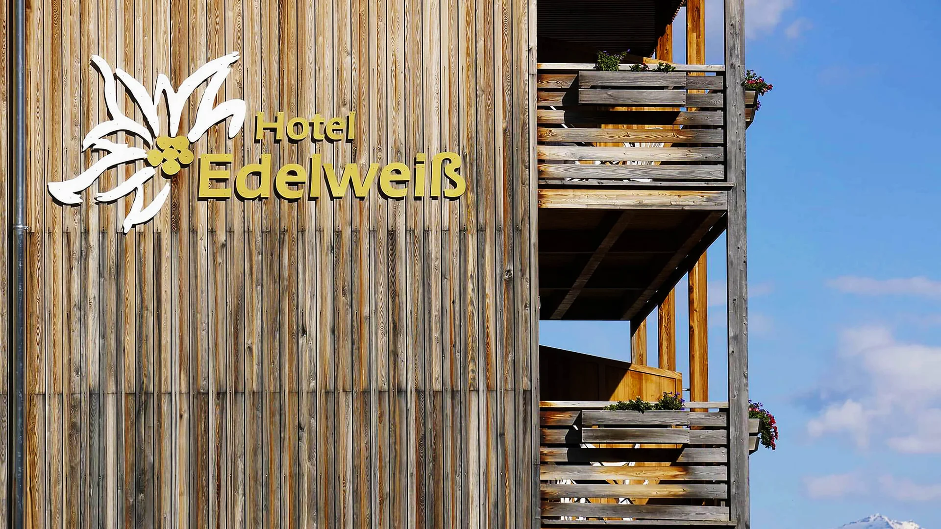 Holzfassade des Hotels Edelweiss mit Balkonen und verschneitem Berg im Hintergrund