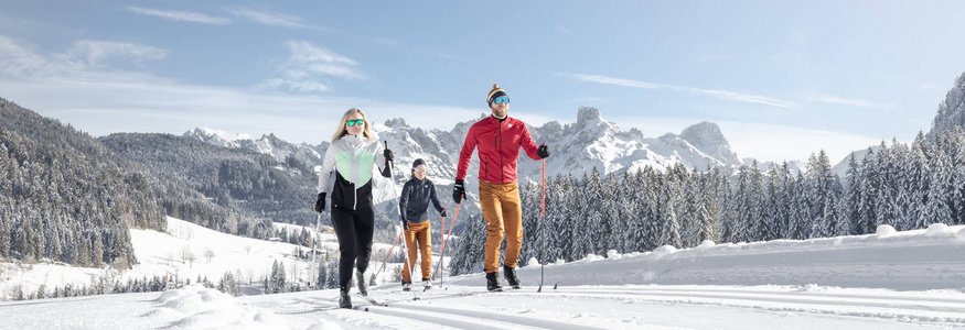 Tennengau © Dachstein West Drei Personen beim Langlaufen vor verschneiten Bergen und klarem Himmel.