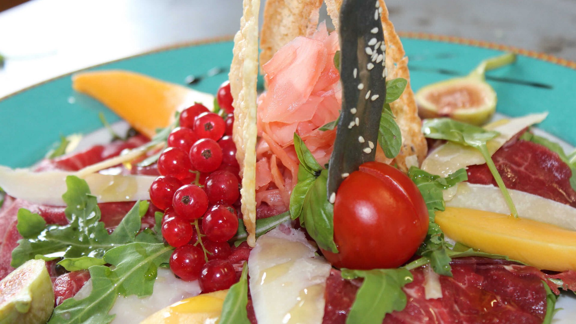 Fein angerichtete Vorspeise mit Rindfleisch, Kirschtomate, Beeren und Rucola