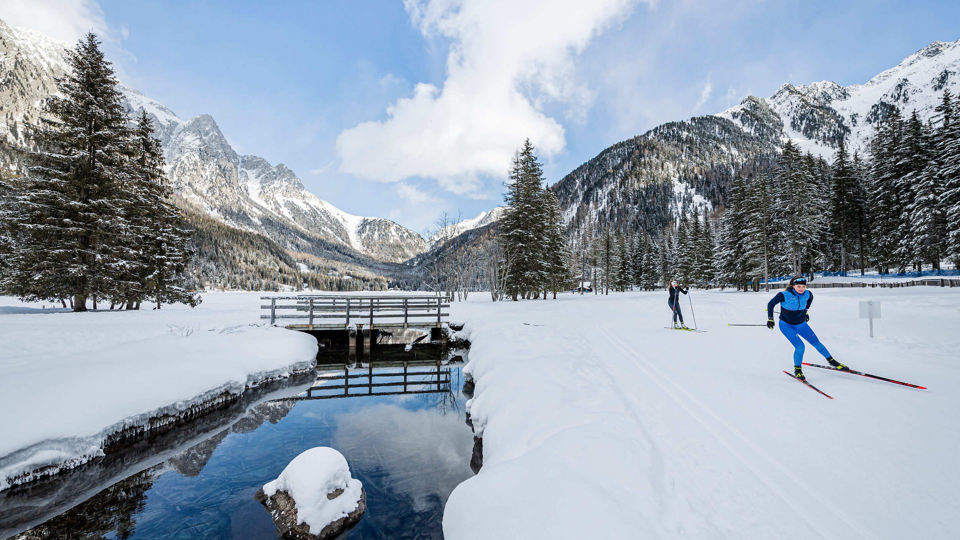 Langläufer unterwegs auf verschneiter Winterlandschaft mit Bergen und Wald
