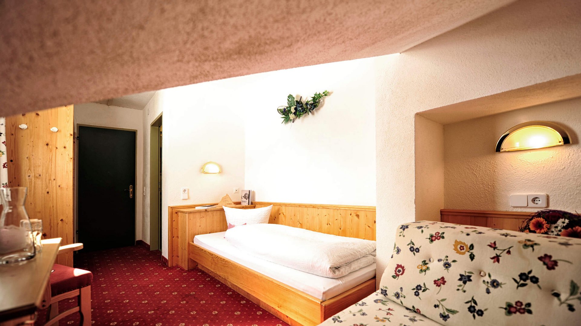 Cozy single room with wooden bed frame and floral-patterned sofa