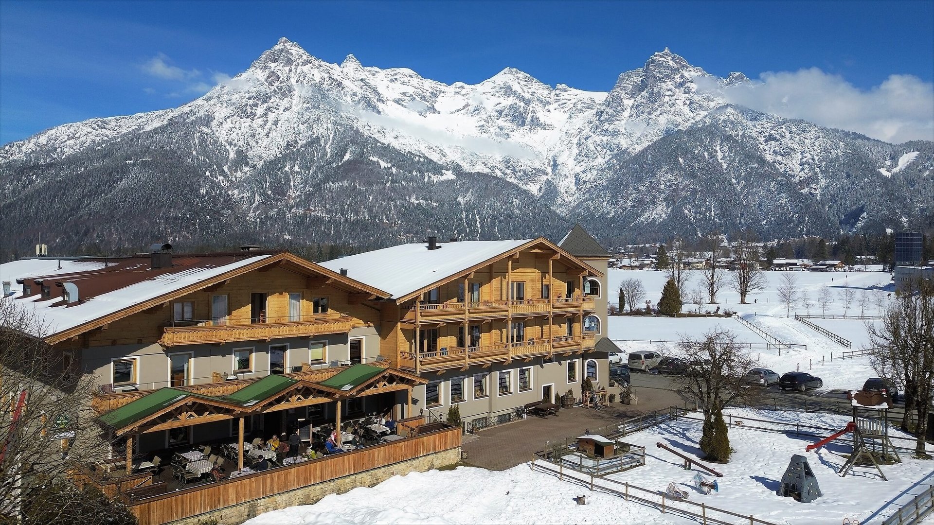 Mountain hotel in front of snowy Alps under clear blue sky