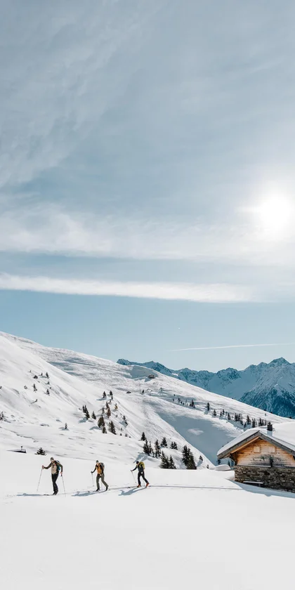 Drei Skifahrer in verschneiter Berglandschaft bei sonnigem Himmel