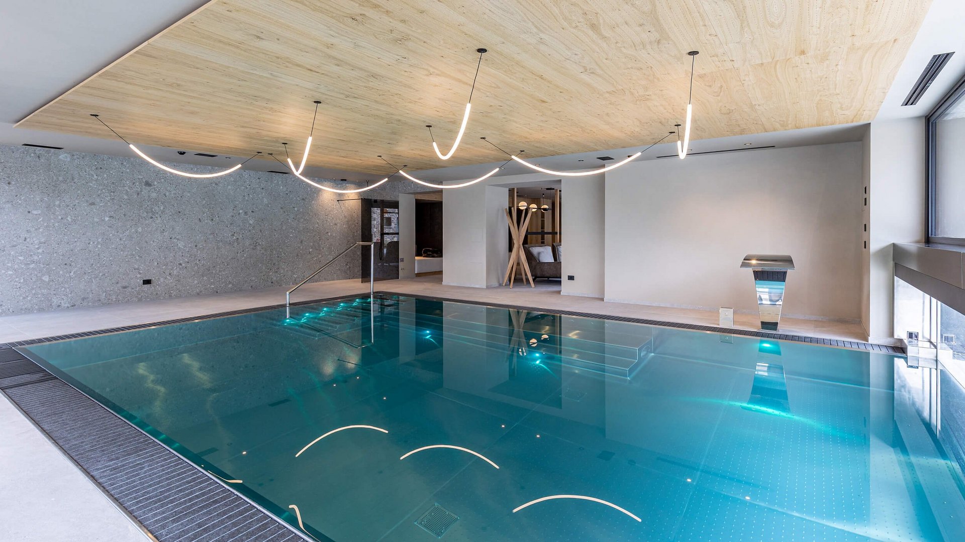 Moderner Innenpool mit Holzbalkendecke und geschwungenen Deckenleuchten