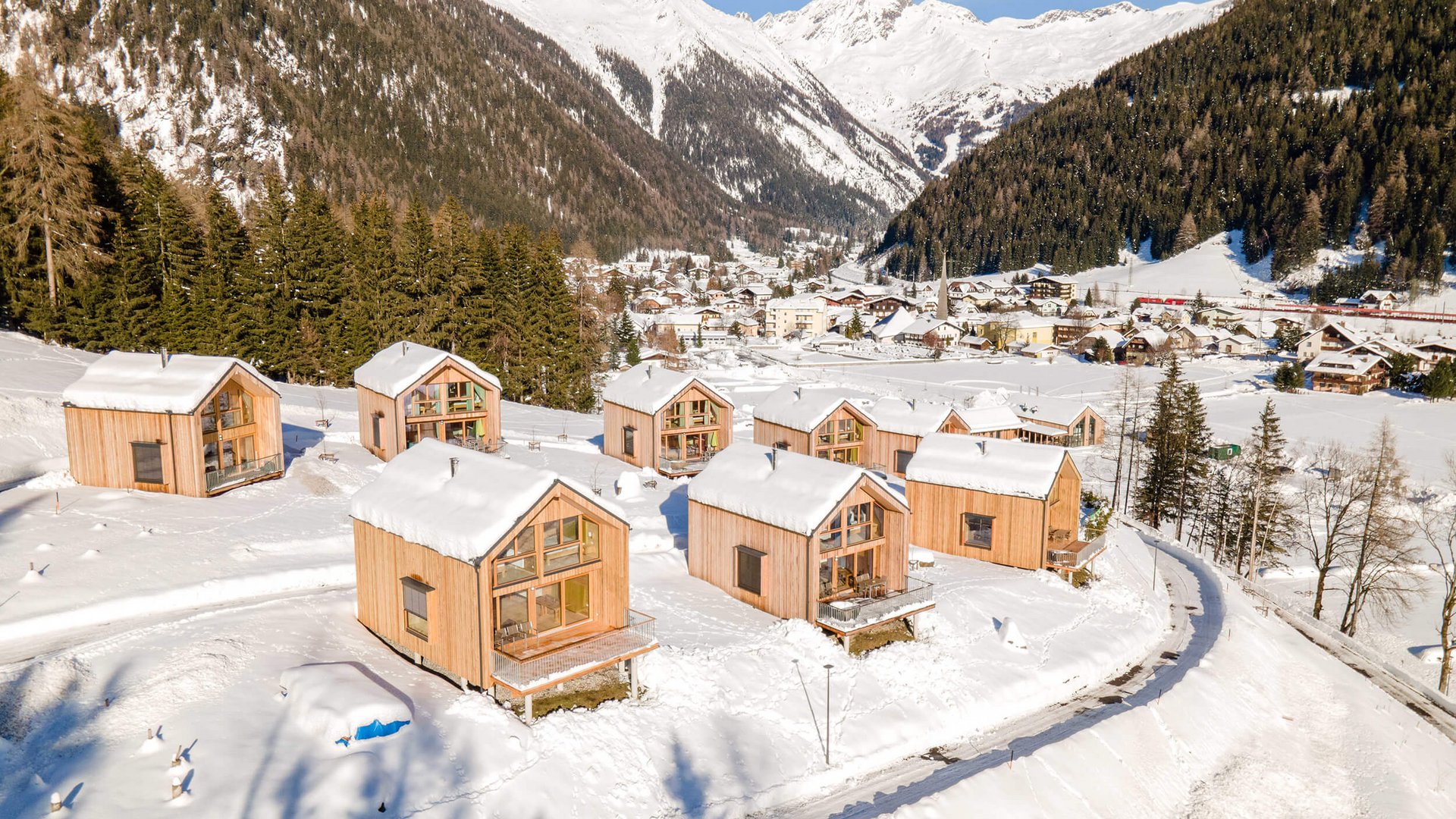 Wooden cabins in snowy mountain landscape with village and mountains beyond