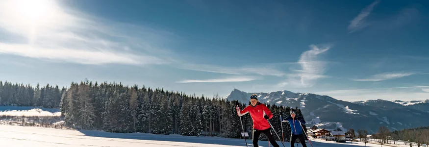 Zwei Langläufer bei sonnigem Winterwetter auf Loipe in Berglandschaft
