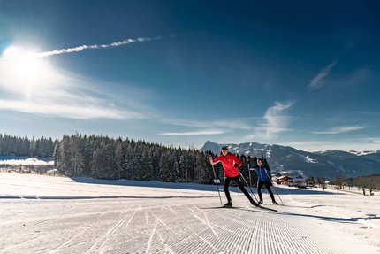 Zwei Langläufer bei sonnigem Winterwetter auf Loipe in Berglandschaft