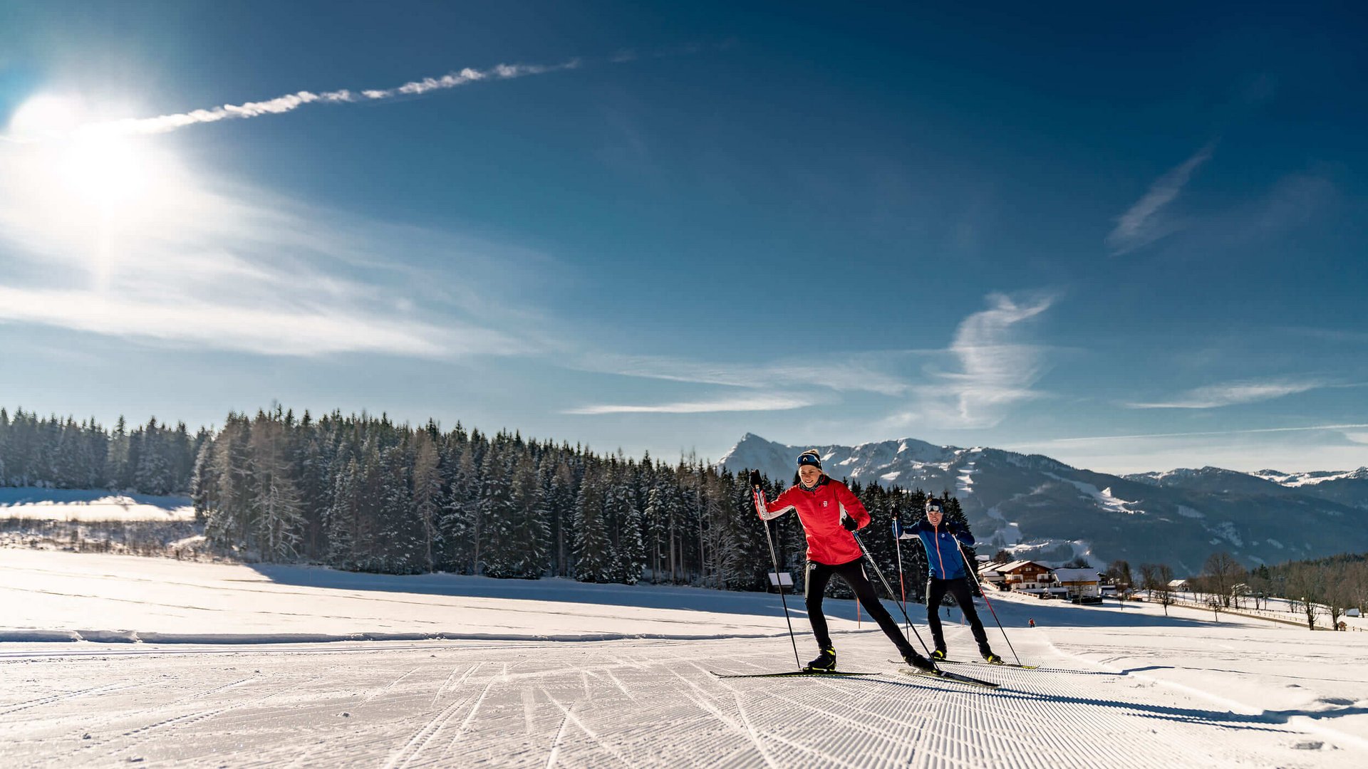 Zwei Langläufer bei sonnigem Winterwetter auf Loipe in Berglandschaft