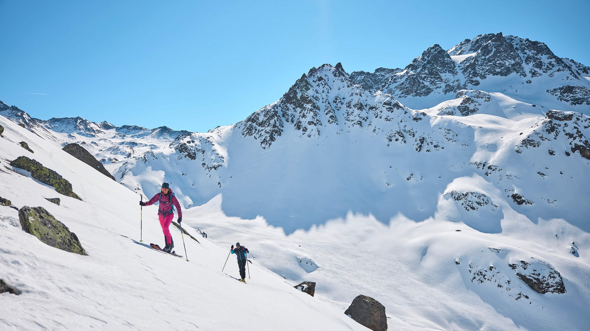 Two ski tourers climbing a snowy mountain slope under clear blue sky