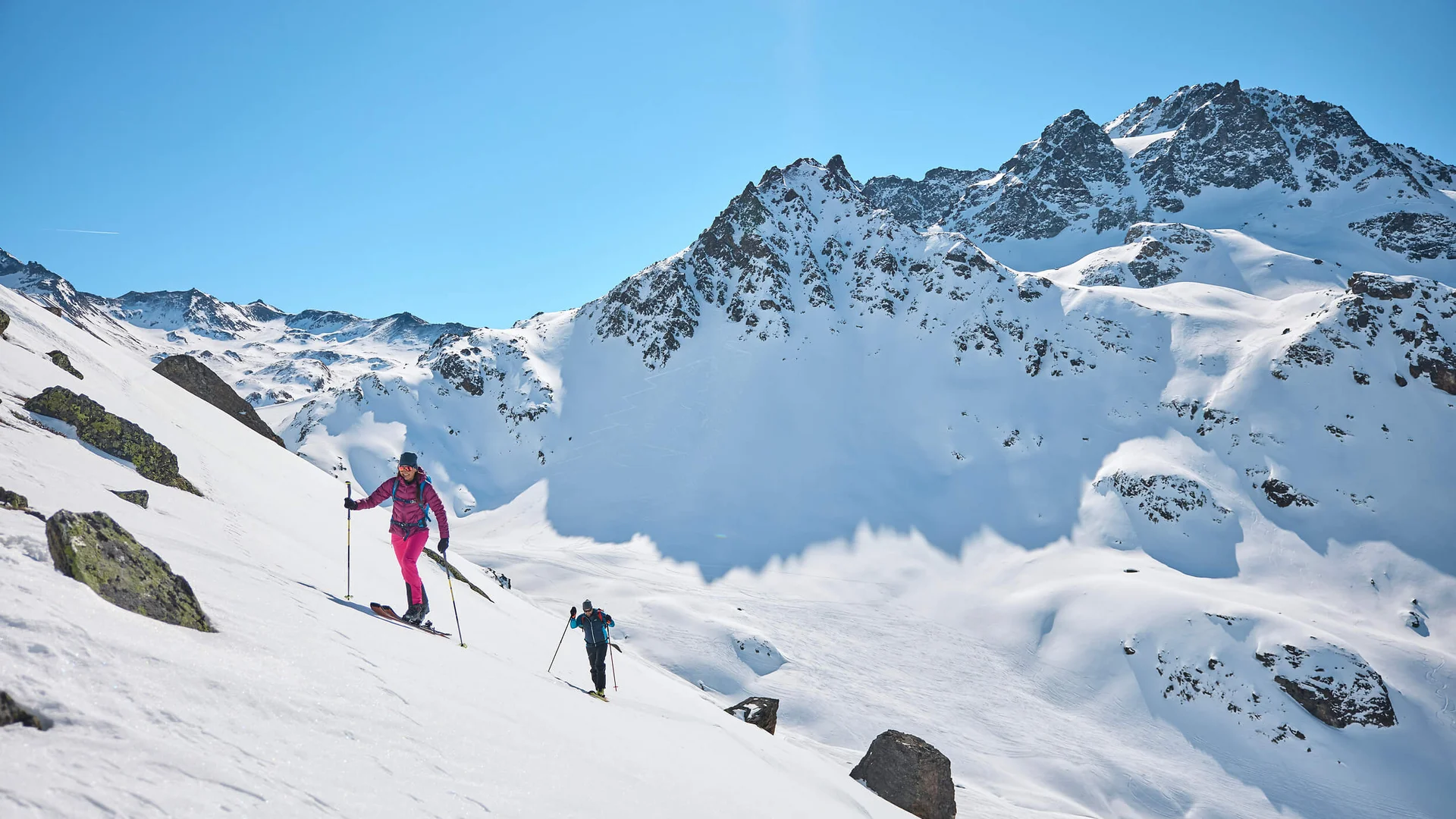Zwei Skitourengeher steigen auf schneebedecktem Berg mit blauem Himmel auf