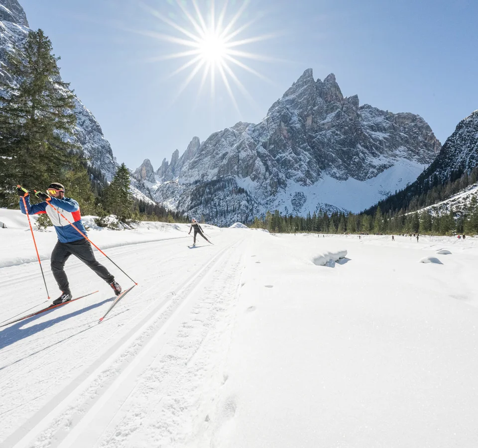 Langläufer im verschneiten Gebirgstal bei strahlendem Sonnenschein